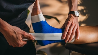 Rechter Fuß einer Patientin wird von Physiotherapeut von PhysioSport Köln getaped.