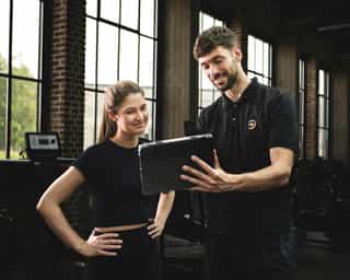 Trainer bei Erläuterung von Trainingskonzept am Tablet mit einer Patientin.