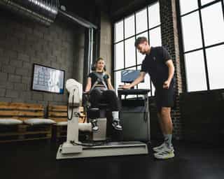 Trainer von PhysioSport Köln erläutert Sportlerin Kraftübungen für die Beinmuskulatur.