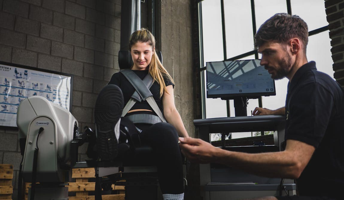 Trainer von PhysioSport Köln erläutert Sportlerin Kraftübungen für die Beinmuskulatur.