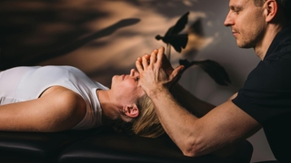 Patientin bei PhysioSport liegt entspannt auf Liege, Therapeut behandelt osteopathisch Kopf- und Stirnbereich.