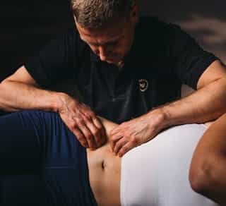 Physiotherapeut bendelt liegende Patientin mit Hilfe von Osteopathie im Rumpfbereich.