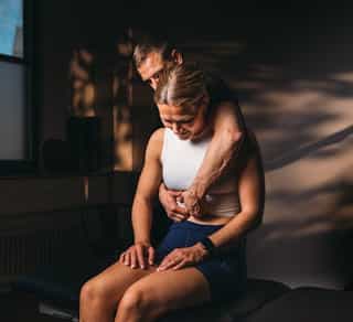 Osteopathie bei PhysioSport Köln: Patientin sitzt, Therapeut behandelt die Wirbelsäule osteopathisch..