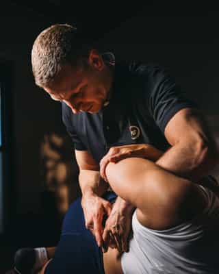 Physiotherapeut von PhysioSport Köln mobilisiert die Schulter einer Patientin.