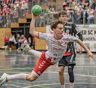 Das Bild zeigt eine Szene aus einem Handballspiel der Herrenmannschaft vom Longericher SC Köln, den Partnern von Physiosport Köln. Zu sehen sind Spieler auf dem Spielfeld und Zuschauer im Hintergrund.