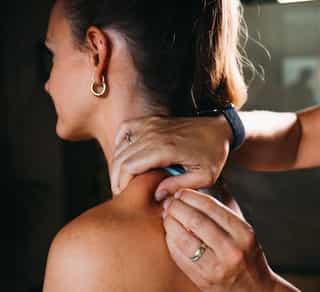 Patientin auf Liege sitzend, Therapeutin lokalisiert bei PhysioSport die Punkte für Dry Needling Behandlung am Rücken.