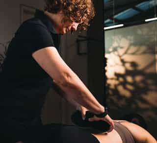 PhysioSport Köln: Mitarbeiterin legt Patientin auf der Liege Wärmekissen für Physikalische Therapie auf.