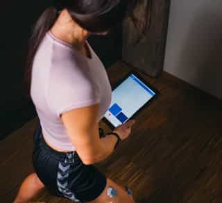 Patientin bei PhysioSport während einer Physikalischen Therapie mit EMG, Elektroden am Oberschenkel und Gerät in der Hand.