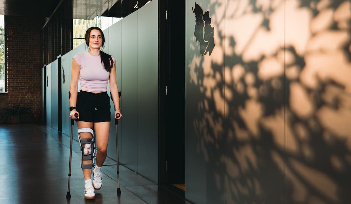 Junge Sportlerin mit Krücken und Kneebrace auf dem Weg zur Behandlung bei PhysioSport Köln.