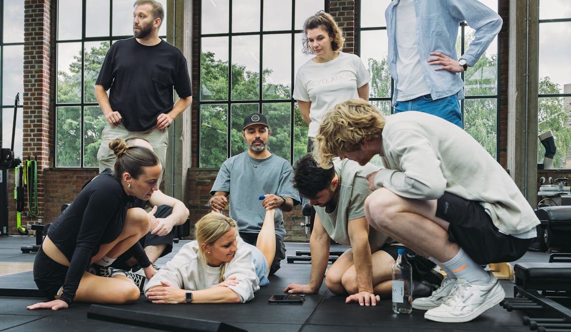Gruppe von Patient:innen mit Physiotherapeut:innen von PhysioSport Köln bei einer Besprechung in der Trainingshalle