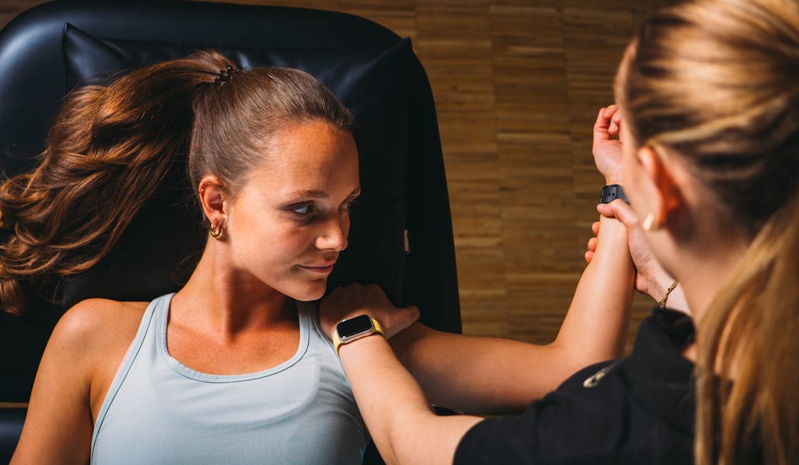 Zu sehen ist eine Physiotherapeutin von PhysioSport Köln bei der Behandlung einer Patientin mit Impingement Schulter. Die Patientin liegt dabei flach auf dem Rücken.