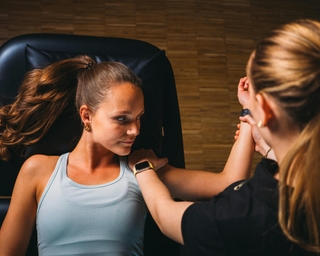 Zu sehen ist eine Physiotherapeutin von PhysioSport Köln bei der Behandlung einer Patientin mit Impingement Schulter. Die Patientin liegt dabei flach auf dem Rücken.