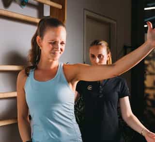 Zu sehen ist eine Sportlerin bei der Beschwerdeanalyse durch eine Physiotherapeutin von PhysioSport Köln.