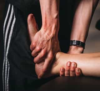 Physiotherapeut von PhysioSport Köln behandelt eine Sportlerin mit manueller Therapiea m rechten Fuß.